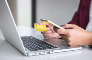 Open laptop with one hand holding a phone and other hand holding a credit card.
